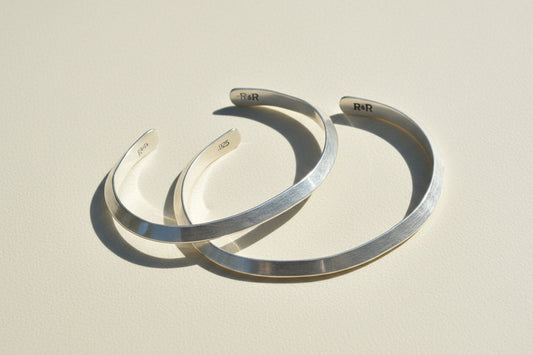 Pair of silver cuff bracelets, open V design with engraved inner logos