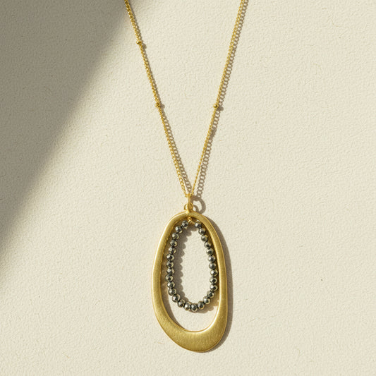 Oval pyrite-bead pendant necklace with gold chain and oval metal frame