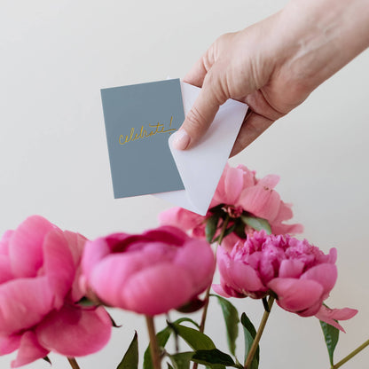Mini greeting card on blue cover held above pink flowers
