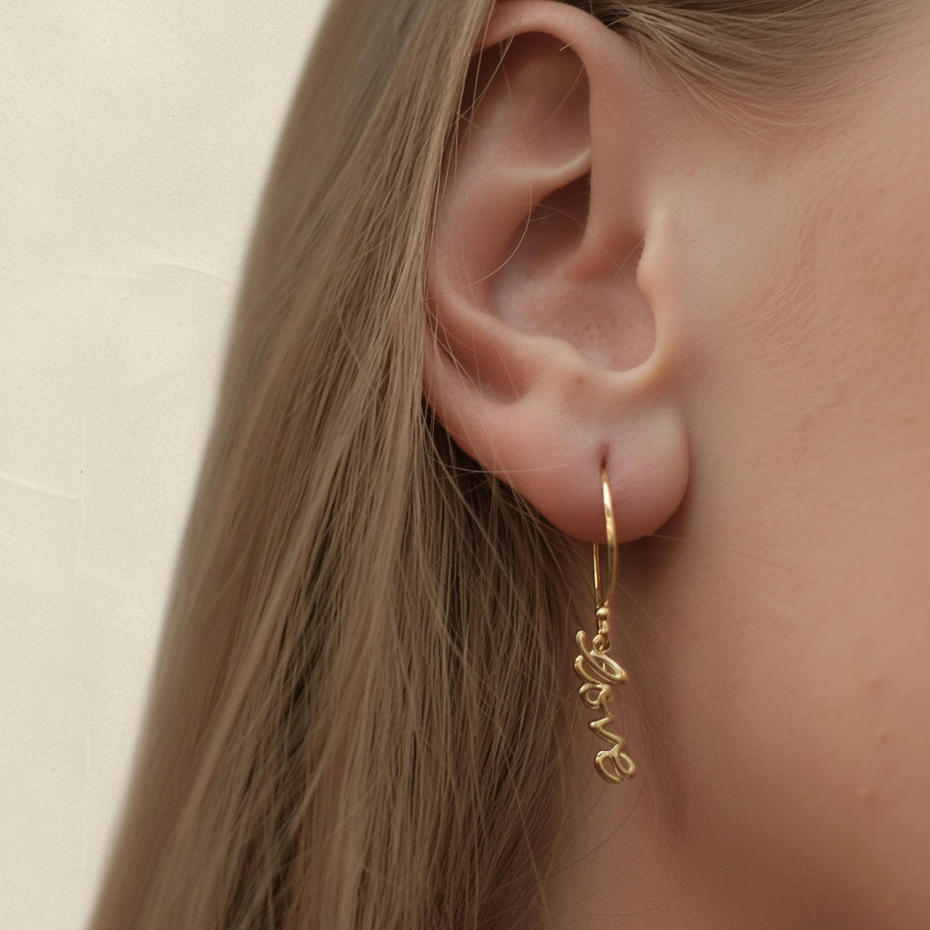 Gold script dangle earrings worn on ear, with hoop and love charm