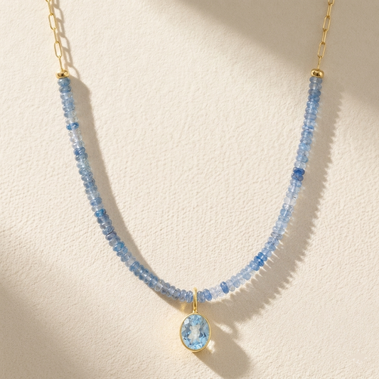 Gold-toned beaded paperclip necklace with light blue stones and round blue pendant