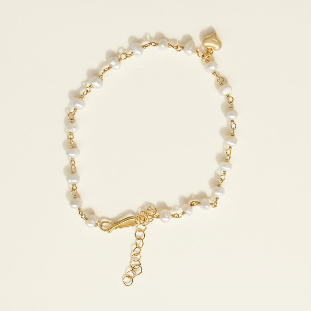 Gold bracelet with pearl beads and a heart charm on a white background