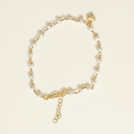 Gold bracelet with pearl beads and a heart charm on a white background