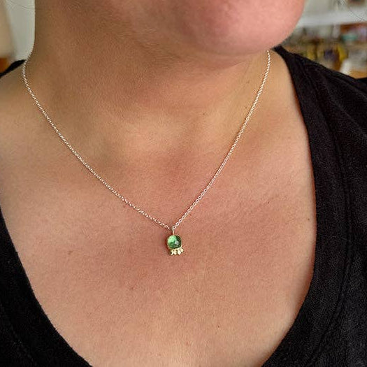 Silver chain necklace with small green gemstone pendant at collar