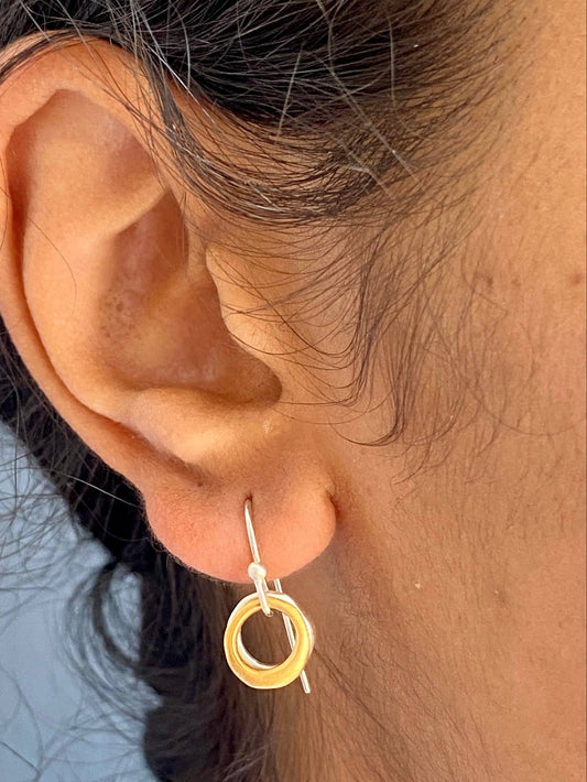 Two-tone circle charm hoop earrings, gold outer ring with silver inner ring, on ear