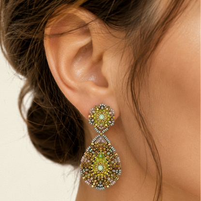 Close-up of a woman's ear wearing a decorative earring with green gemstones.