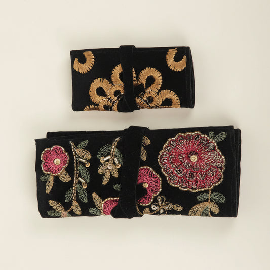 Black jewelry roll with gold floral embroidery; pink flower accents, rolled and tied.