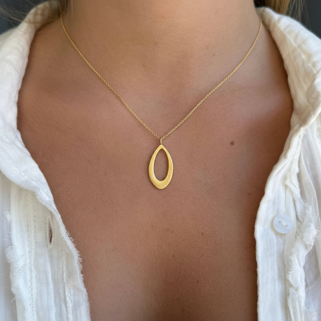Gold leaf-shaped pendant on fine chain, worn on neckline with white blouse