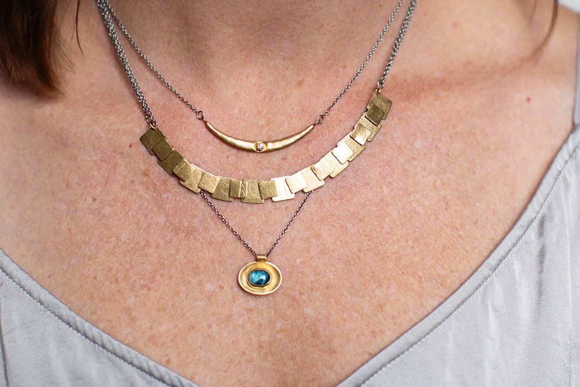 Oval necklace with silver and gold chain, blue oval pendant at center