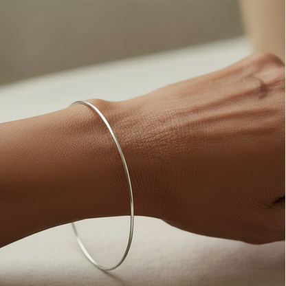 Thin silver bangle bracelet on wrist, smooth oval cuff