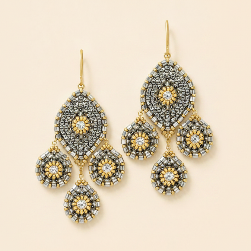 A pair of ornate gold and silver-tone dangle earrings with intricate floral and geometric patterns, displayed on a solid light beige background.