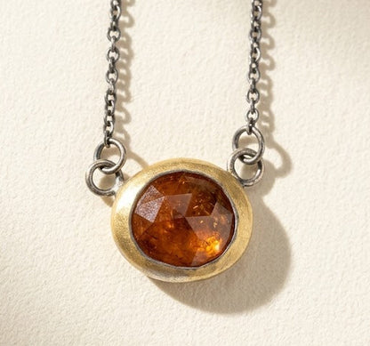 Amber round gemstone pendant necklace with gold-toned rim and dark chain, close-up