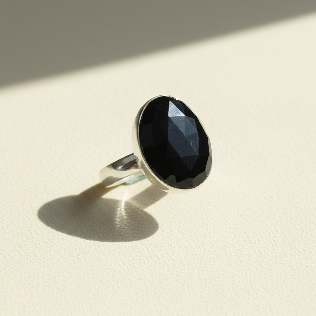 Black oval faceted gemstone set in silver ring band, side view