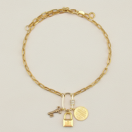 Gold-tone charm necklace with lock, key, and round coin pendant on curb chain
