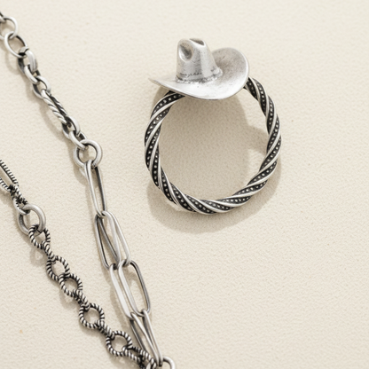 Cowboy hat ring featuring silver hat top and twisted rope band, near chain links
