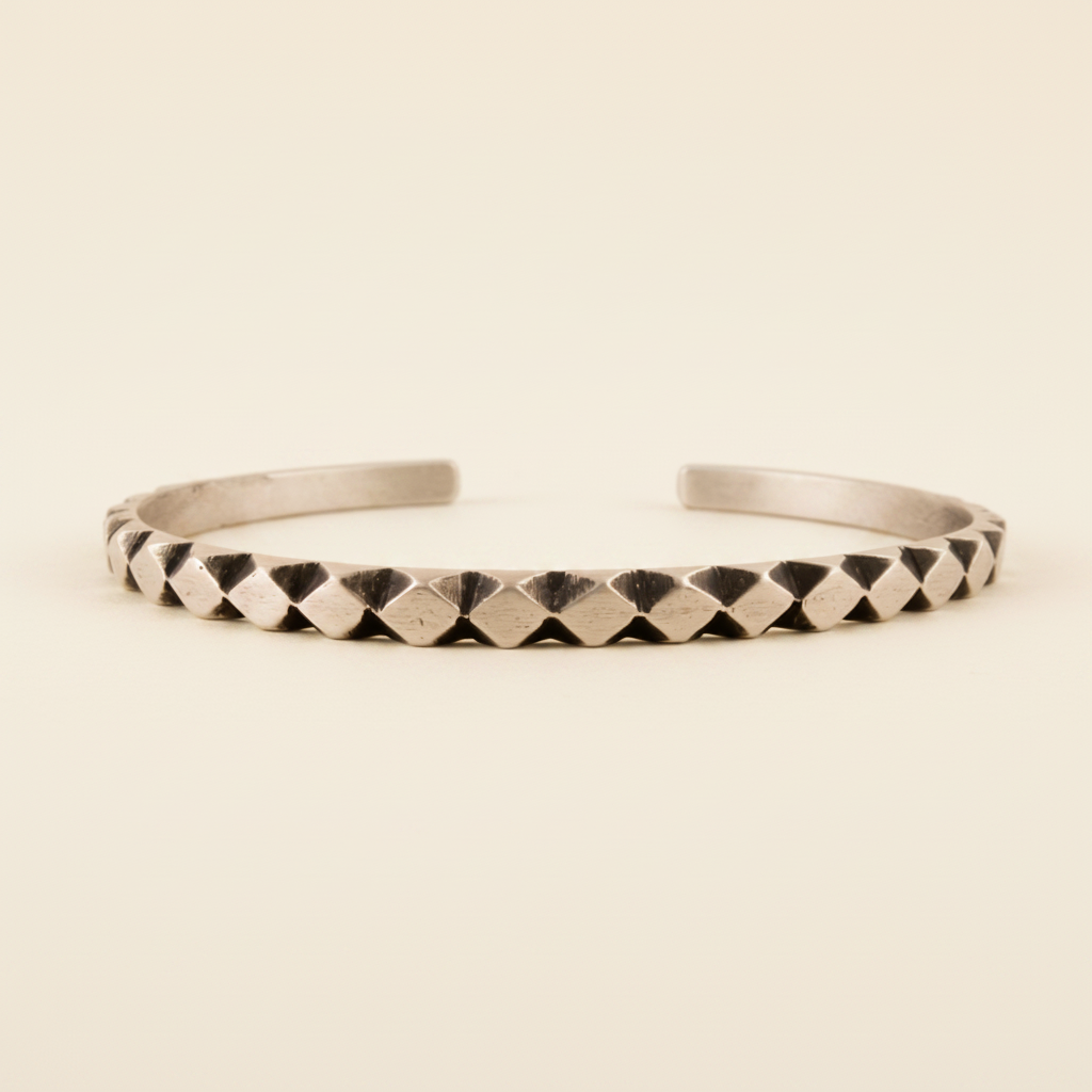 Silver-toned cuff bracelet with carved diamond texture and dark geometric accents