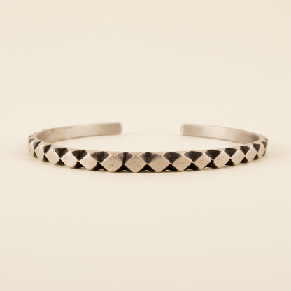 Silver-toned cuff bracelet with carved diamond texture and dark geometric accents