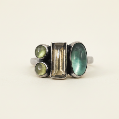 Multi-stone ring with rectangular center and three green-toned stones in dark settings