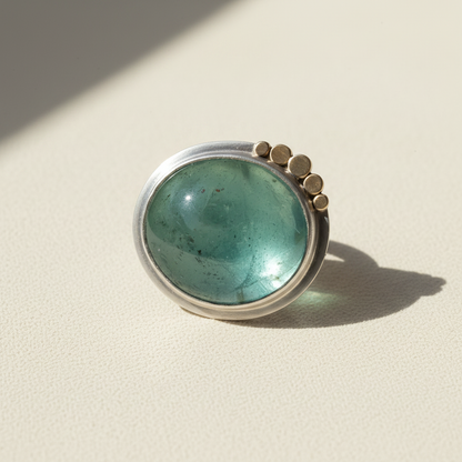 Round green gemstone cabochon ring with silver bezel and small gold-tone accents