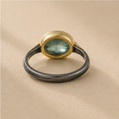 Two-tone apatite ring front view: oval blue-green stone, gold top bezel, dark silver band