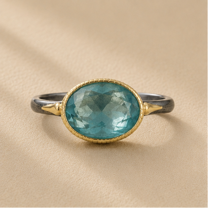 Two-tone apatite ring with oval blue-green stone and gold bezel on dark silver band