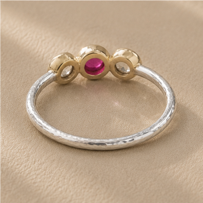 Silver ring with gold crown, pink center ruby, and two side cool-toned round stones
