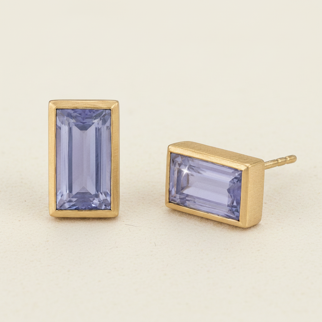 Gold earrings with rectangular purple gemstones on a white background