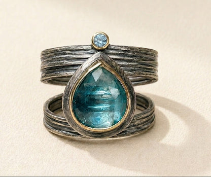 Silver cuff-style ring with large teal teardrop gemstone and small round blue stone
