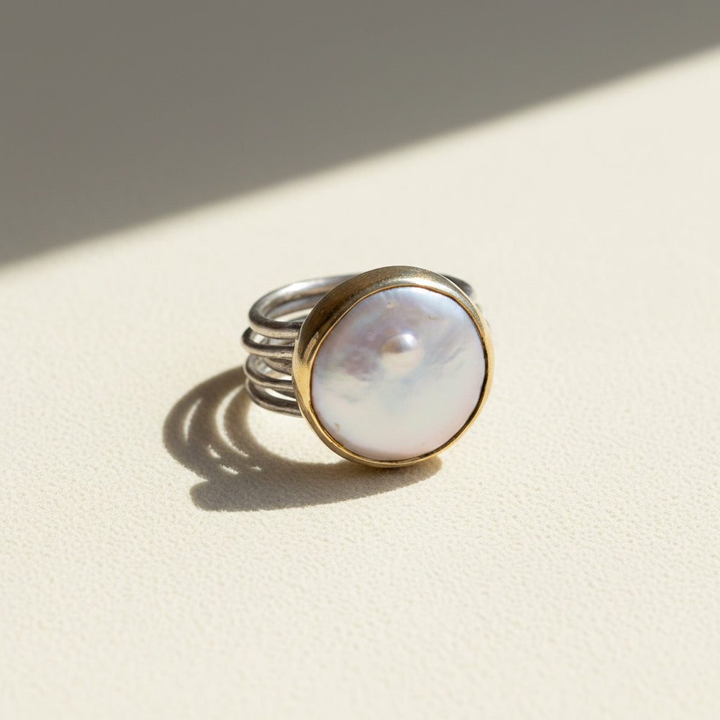 Nomad dancing pearl ring with opalescent round pearl, silver band, and gold bezel